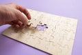 a hand holding a jigsaw piece and complete puzzle on the table