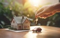 Hand holding keys next to a house and a car models representing home and real estate ownership, loan, mortgages and debt Royalty Free Stock Photo