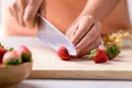 Hand holding kitchen knife and cutting strawberry on wooden board