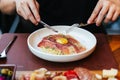 Hand holding knife and fork for eating Fettuccine Carbonara with parma ham and yolk with black pepper. Served in white plate Royalty Free Stock Photo