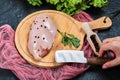 Hand holding knife and piece of raw chicken fillet on wooden plate with fresh vegetables and tablecloth Royalty Free Stock Photo