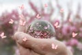 Hand holding a lens ball reflecting pink flowers