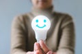 Hand holding a light bulb with smiley face icon. Satisfaction survey and customer service concept.