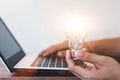 Hand holding a light bulb and working on a laptop computer. Royalty Free Stock Photo