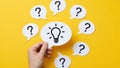 Hand holding a lightbulb idea symbol amidst question marks Royalty Free Stock Photo