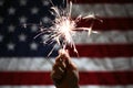 Hand holding sparkler in front of the American Flag for 4th of July celebration