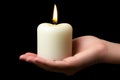 hand holding lit white candle against black background, symbolizing warmth and tranquility Royalty Free Stock Photo