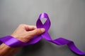 A hand holding luxury purple ribbon on a gray background.