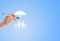 Hand holding magic pen and drawing white umbrella above family icon for protection.