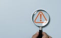 Hand holding magnifier glass with red triangle caution warning sign for focus notification error and maintenance concept Royalty Free Stock Photo