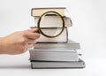 Hand holding magnifying glass and books stack. Reading, data search and analysis concept