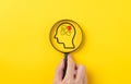 Hand holding magnifying glass focusing on human brain jigsaw puzzle on yellow background. human psychology or mental health or Royalty Free Stock Photo