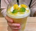 Hand holding mango smoothie cup on wooden table