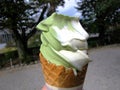 A hand holding melting ice cream waffle cone in hand, green tea matcha, vanilla, on summer , blurry background,