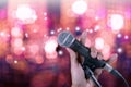 Hand holding microphone on stand with bokeh .