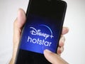 Hand holding mobile phone with finger touch the Disney Hotstar logo on screen.
