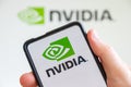 Hand holding a mobile phone with Nvidia logo of the software company which designs graphics processing units GPU computer screen