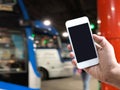 hand holding mobile phone over blur background of bus platform at night