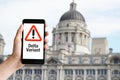 Hand holding mobile phone with with warning message delta variant and historic building at Liverpool Royalty Free Stock Photo
