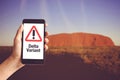 Hand holding mobile phone with warning message delta variant and Uluru mountain in Australia Royalty Free Stock Photo