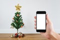 Hand holding mobile smart phone, blank white screen with Christmas tree decoration in living room background Royalty Free Stock Photo