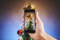 Hand holding mobile smart phone, taking photo of Christmas star on Christmas tree with colorful lights Royalty Free Stock Photo