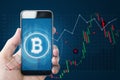 Hand holding mobile smartphone with B symbol of Bitcoin, internet banking and block chain on screen and raising graph background