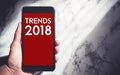 Hand holding mobile with trends 2018 on phone screen with sunlight from window at white marble wall,Business vision for new Royalty Free Stock Photo