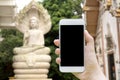 Hand holding mockup white mobile phone to taking a photo the stone statue buddha with blank black screen at the temple in Thailand Royalty Free Stock Photo