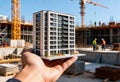 Hand holding model building in construction site with cranes and workers in background Royalty Free Stock Photo