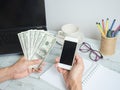 Hand hold money dollar and mobilephone with workspace on white wood table background Royalty Free Stock Photo