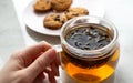 Hand holding mug with herbal tea on marble table and cookie with chocolate chip on pink dish on background. Sweet fast breakfast