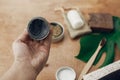 Hand holding natural charcoal toothpaste in glass jar on background of bamboo toothbrush, soap, solid shampoo, metal razor, Royalty Free Stock Photo