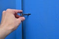 A hand is holding an old key in the keyhole. Blue, metal door with a textured surface. Royalty Free Stock Photo