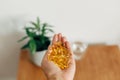 Hand holding omega 3 capsules above wooden table with glass of water. Morning dose of vitamin. Fish oil in pills. Health support