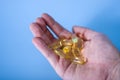 Hand holding omega-3 capsules on a blue background. Palm up, close-up. A high-resolution product