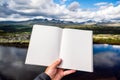 Hand holding a open book with blank and empty pages towards beautiful mountain scenery Royalty Free Stock Photo