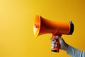 Hand holding orange megaphone against yellow background