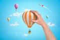 Hand holding orange white hot air balloon with silver rocket and hot air balloons on blue sky background Royalty Free Stock Photo