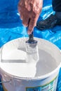 Hand holding a paint brush being dipped into a large tub of white paint ready for use in decorating