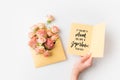 hand holding paper with mothers day phrase beside pink flowers in envelope isolated on white Royalty Free Stock Photo