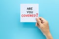 Hand holding paper with question ARE YOU COVERED? isolated on blue background with copy space. travel insurance concept Royalty Free Stock Photo