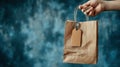 Generative AI Hand Holding Small Paper Bag with Empty Tag on Blue Background for Shopping business concept. Royalty Free Stock Photo