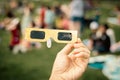 Hand holding paper solar eclipse with blurry crowd people watching totality show picnic yard, Dallas, Texas, April 8