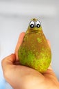 Hand holding a pear with eyes.