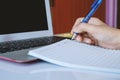 Hand holding a pen to write on notebook and using a computer laptop for working Royalty Free Stock Photo