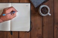 Hand Holding Pen write on notebook with cup of coffee on wooden Royalty Free Stock Photo