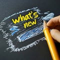 A hand holding a pencil drawing the words what's new on a blackboard Royalty Free Stock Photo