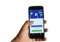 Hand holding Phone with mobile application for Facebook on a white background.