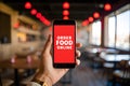 Hand holding phone open to ORDER FOOD ONLINE app at cozy restaurant